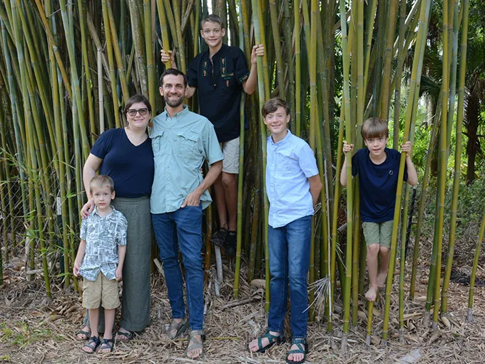Jenny Weigner, a white woman young adult with short brown hair and glasses, with her three sons husband smiling among bamboo trees.