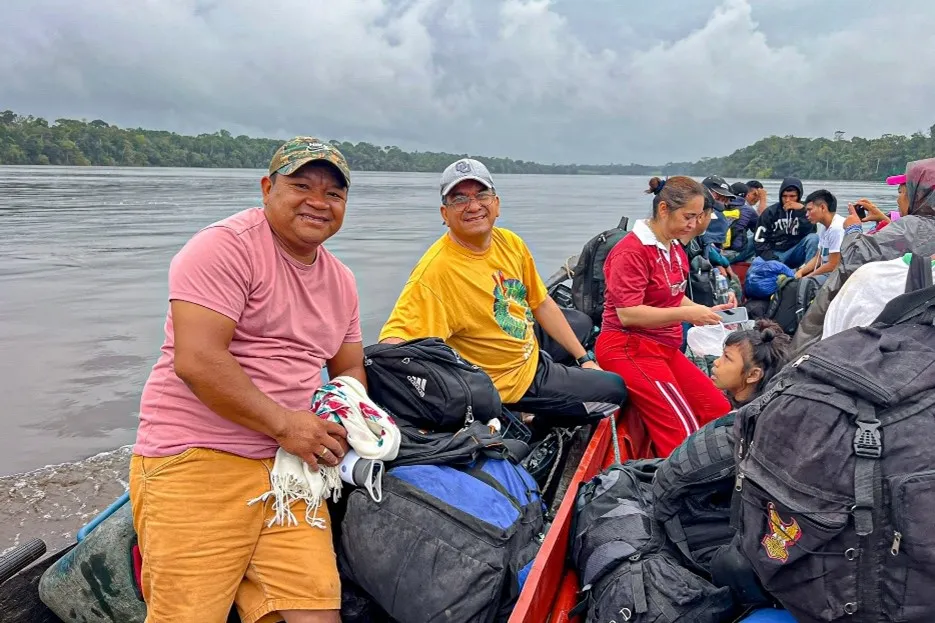Program participants and staff travel by river boat through the Amazonian rainforest for a strategic network visit. The image captures the challenging journey and dedicated people making the trip.