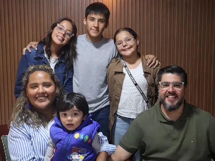 A group photograph features six smiling family members, including parents Luis Salomón (right) and Katy Salomón (seated left), posed together against a simple background.